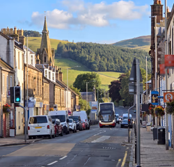 Innerleithen high street, with stone buildings, a church spire and the surrounding hills rising behind